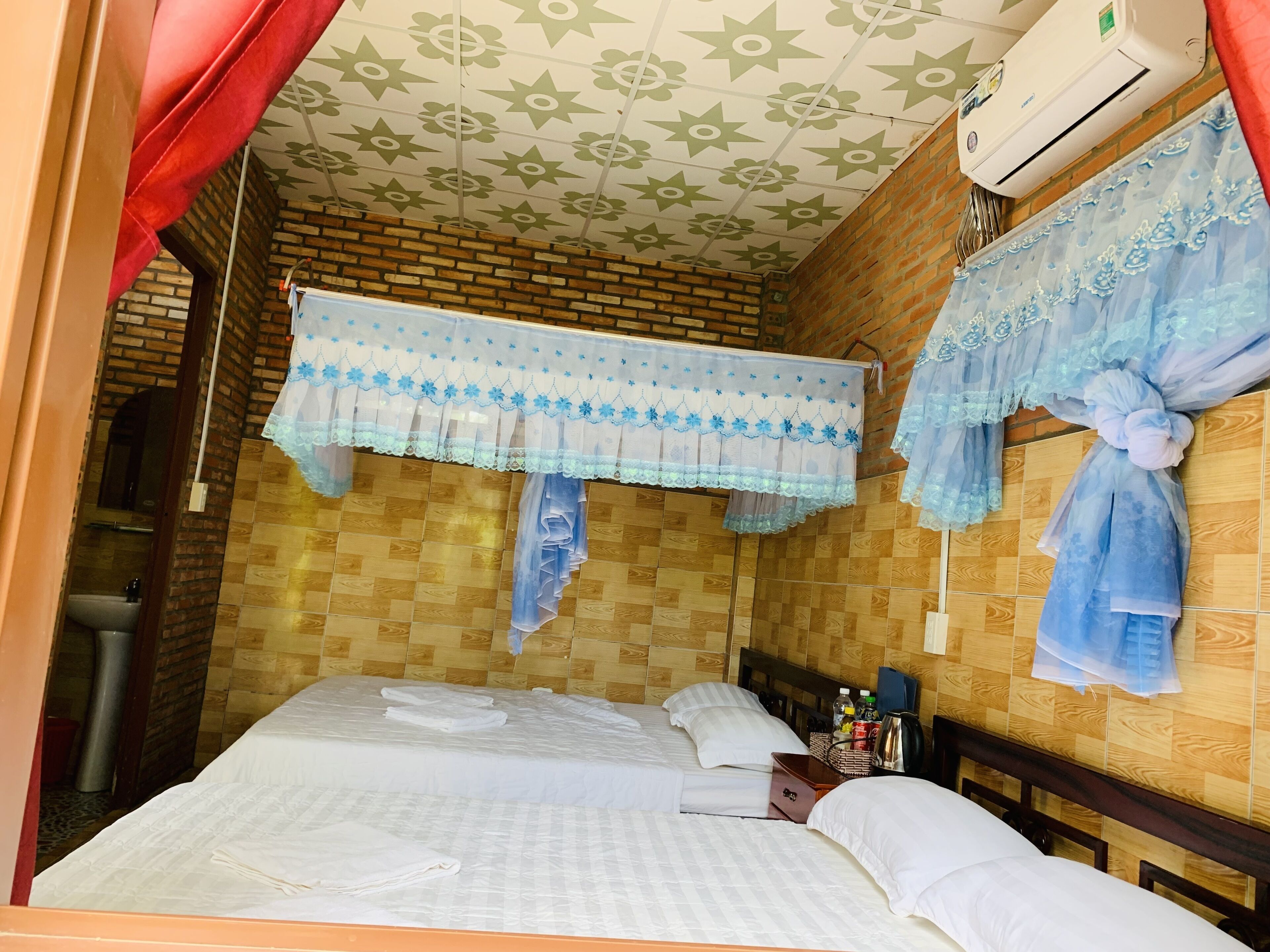Habitación de hotel con cama, cabecera de madera, pared de ladrillo y techo con estampado floral.