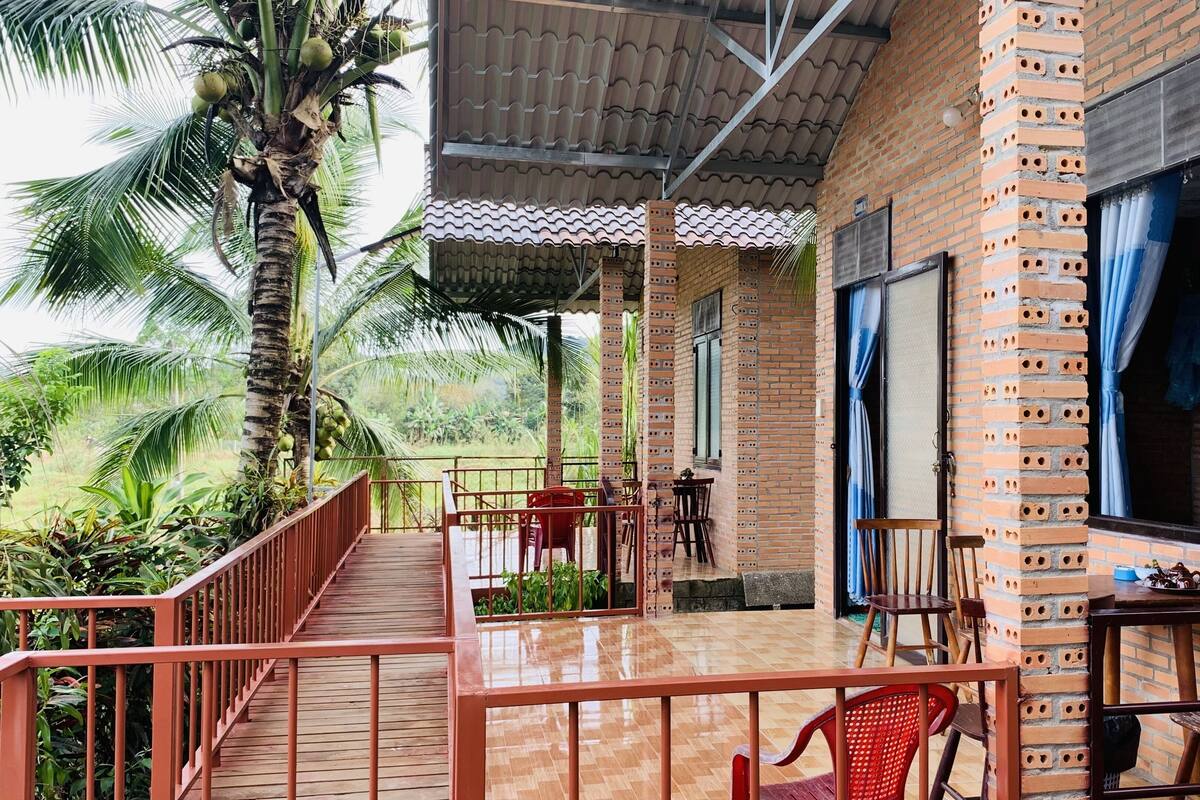 A covered outdoor area with a wooden deck, brick walls, and a view of palm trees.
