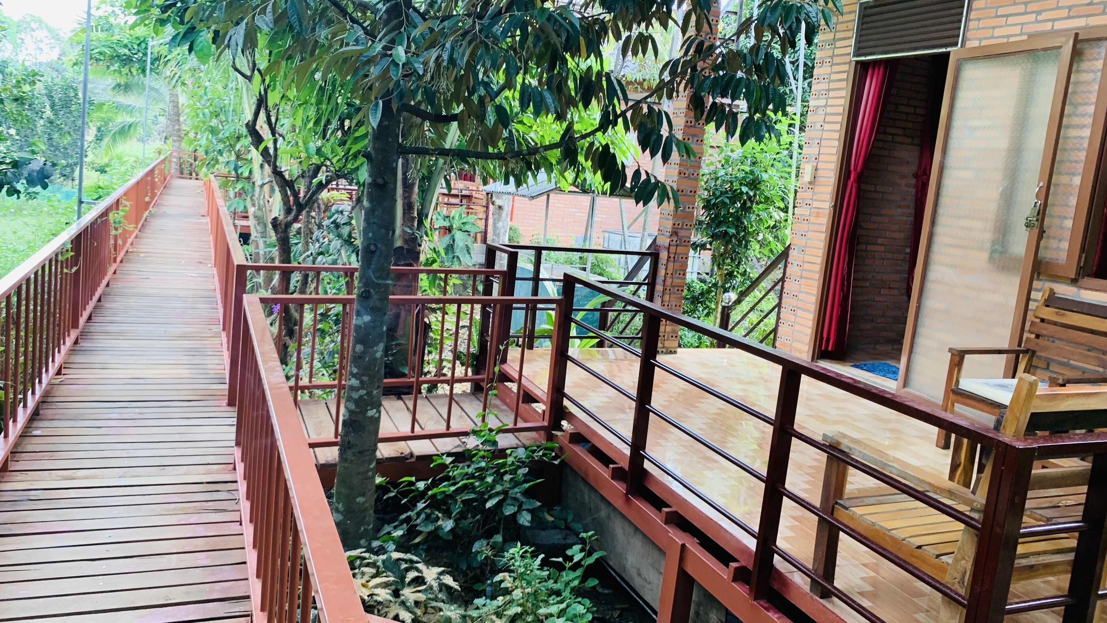 A wooden deck with a metal railing, surrounded by lush greenery and a brick wall.