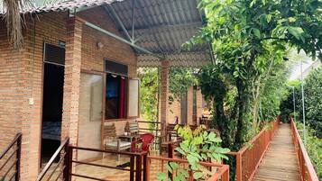 A brick building with a covered porch, a wooden deck, and lush greenery.