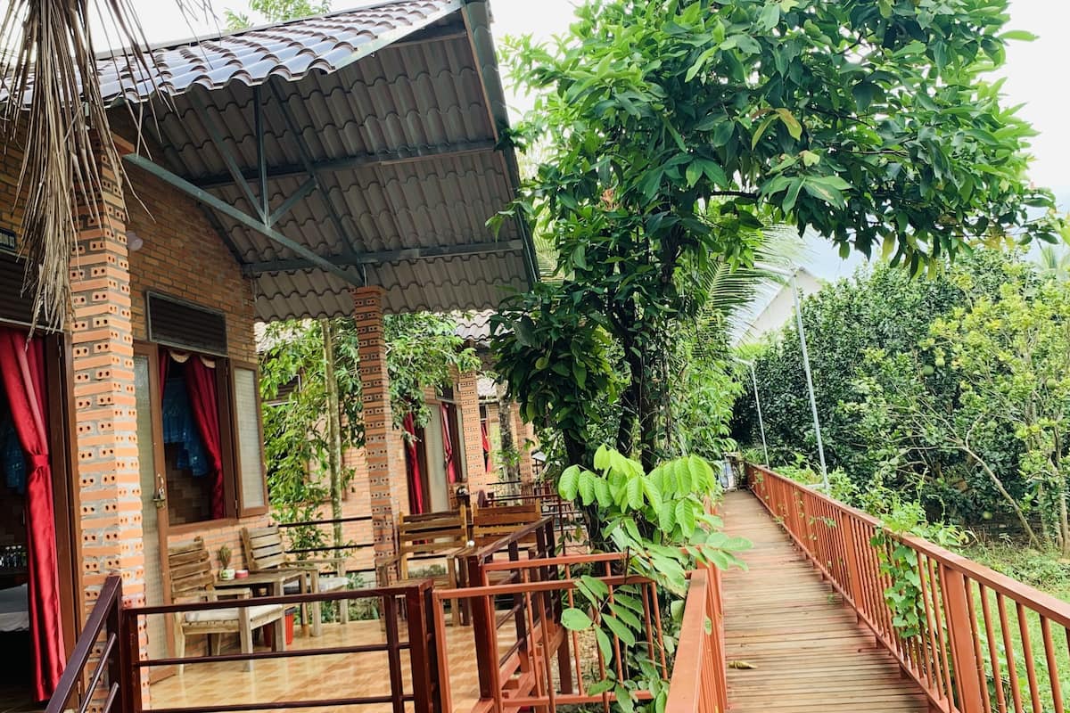 A wooden deck leading to a brick building with a tiled roof, surrounded by lush greenery.