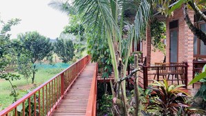 A wooden deck with a red railing leading to a brick building with a window and a door. - Gibbon Singing Homestay (Nam Cat Tien)