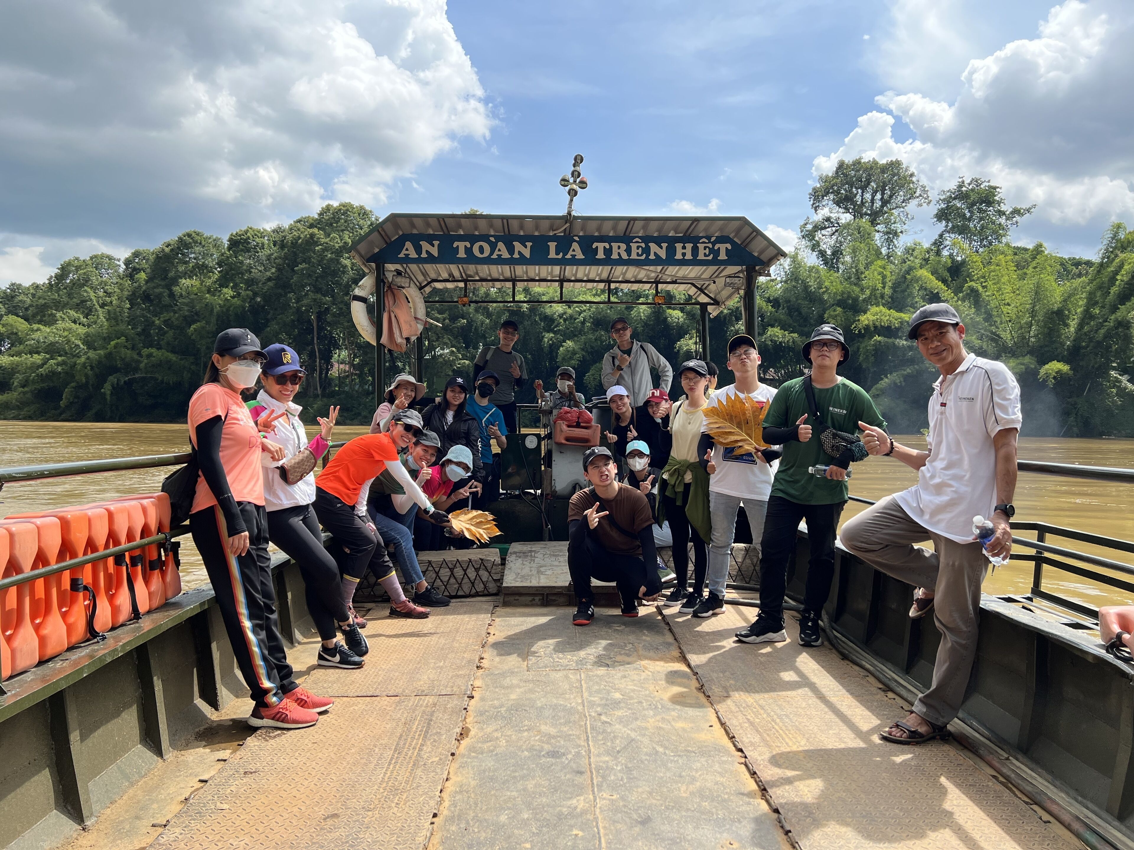 Um grupo de pessoas em um barco, com uma placa com a inscrição "AN TOAN LA TRÊN HỆT" ao fundo.