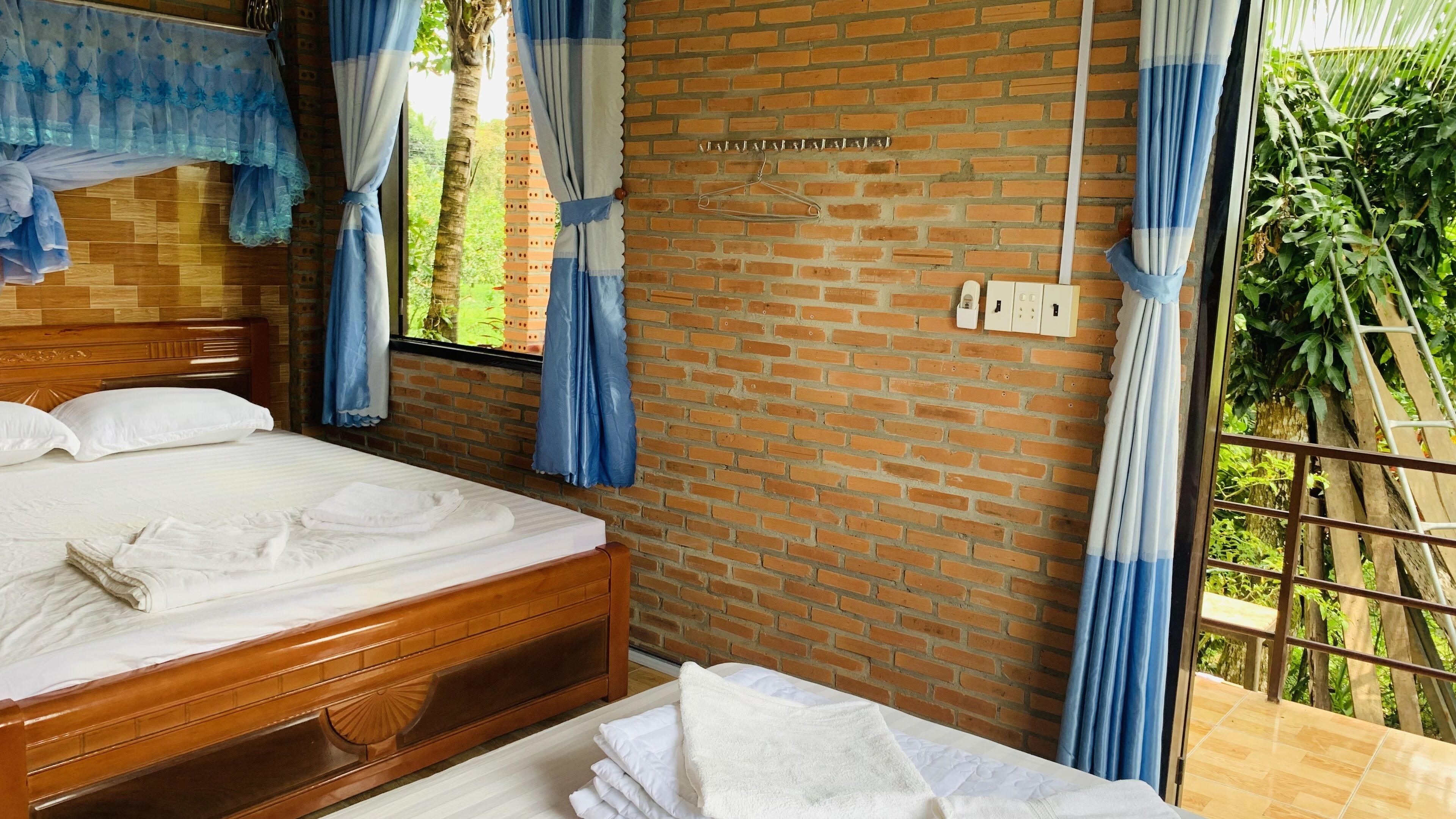 Une chambre avec un lit en bois, un mur en briques et une fenêtre avec des rideaux.