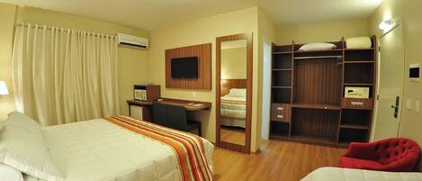 A hotel room with two beds, a desk, a mirror, a wardrobe, and a red chair.