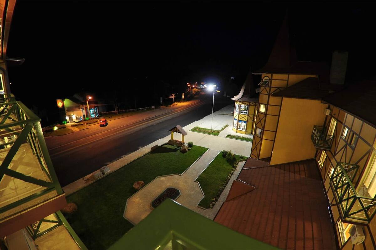 A nighttime view of a street with a well-lit sidewalk, a small gazebo, and a building with a balcony.