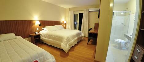 A hotel room with two beds, a desk, a chair, a shower, and a bathroom.
