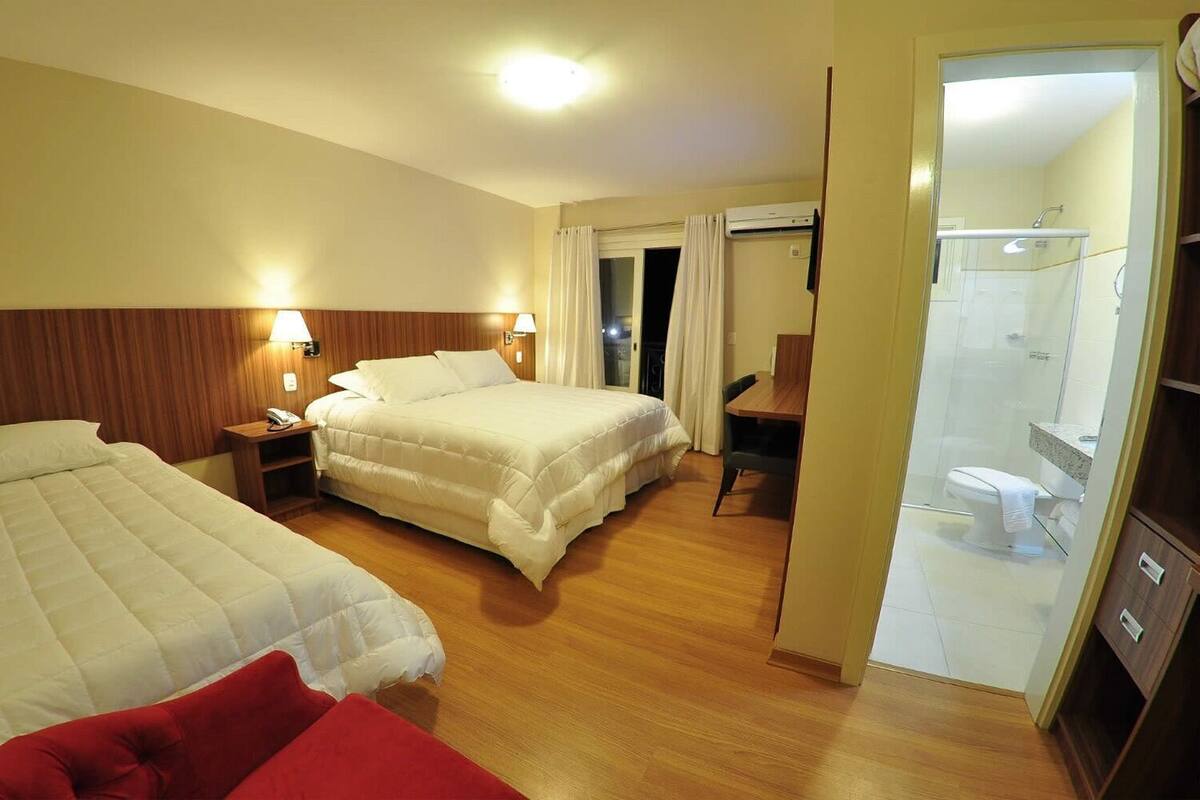 A hotel room with two beds, a desk, a chair, a shower area, and a bathroom.