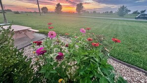 A grassy field with a wooden picnic table and a flower bed with various flowers. - Owensville Motor Inn (Owensville)