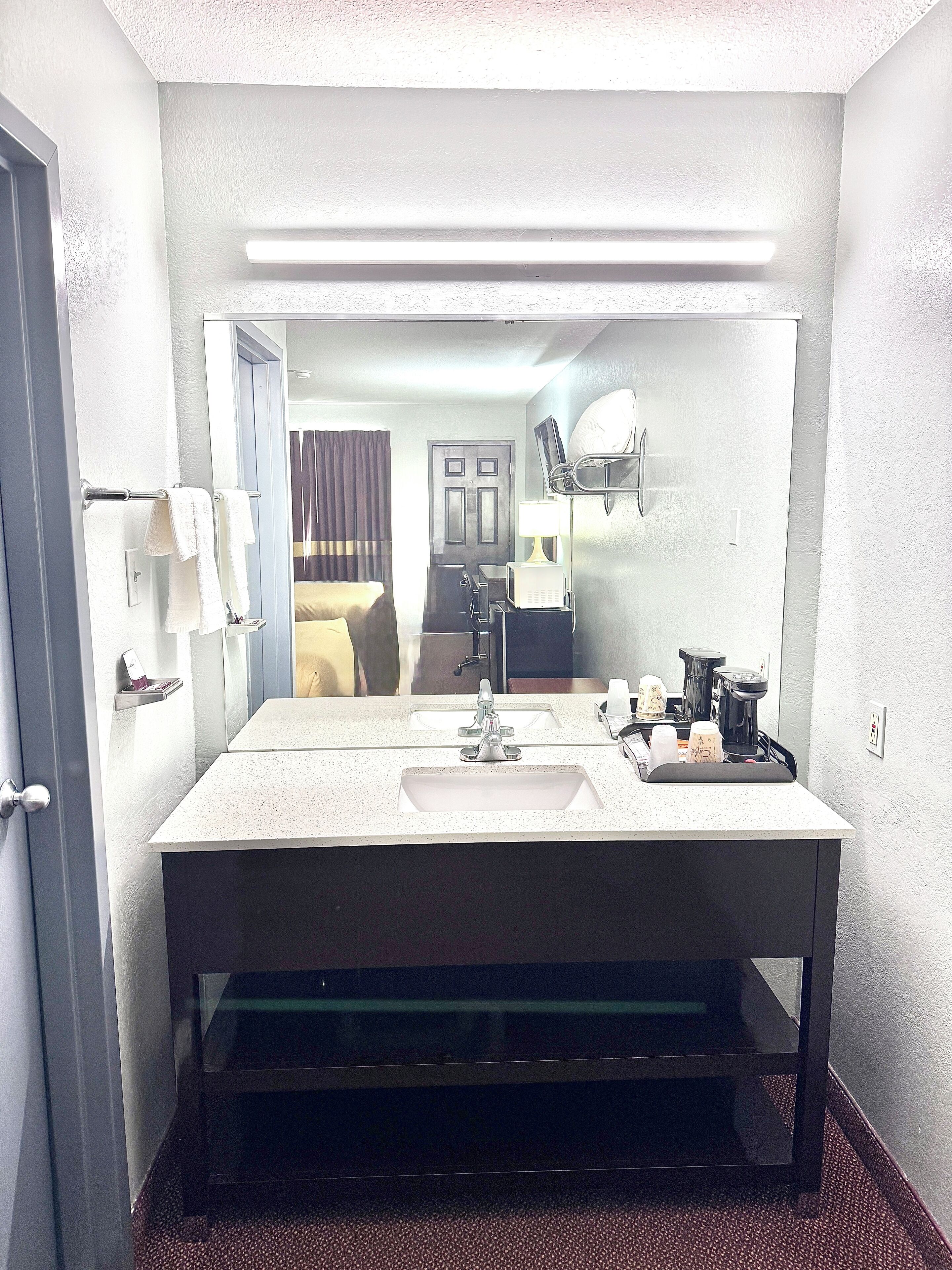 Un baño de hotel con un espejo grande, dos lavamanos, un perchero para toallas, un inodoro y una zona de ducha.
