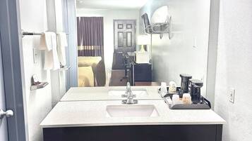 Un baño de hotel con un espejo grande, dos lavamanos, un perchero para toallas, un inodoro y una zona de ducha.