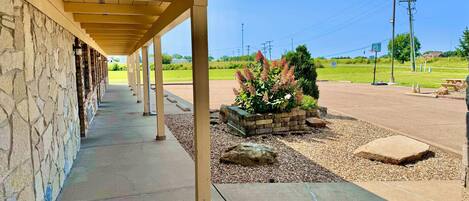 Un espacio al aire libre techado con un muro de piedra, un camino de concreto y una jardinera con plantas.