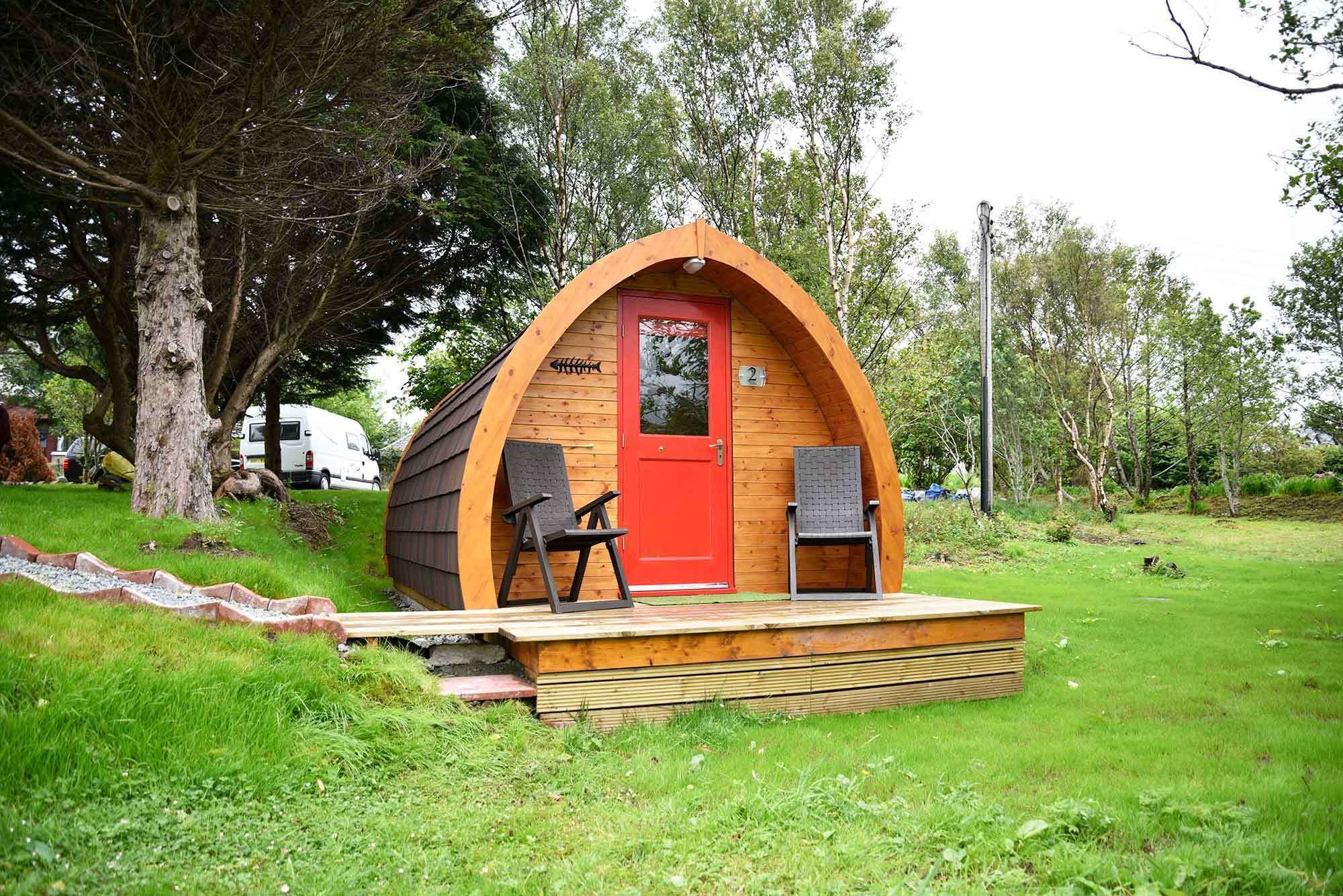 A small, wooden, A-frame structure with a red door and a number '2' sign, surrounded by greenery.
