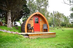 A small, wooden, A-frame structure with a red door and a number '2' sign, surrounded by greenery. - Dunvegan Camping Pods (Dunvegan)