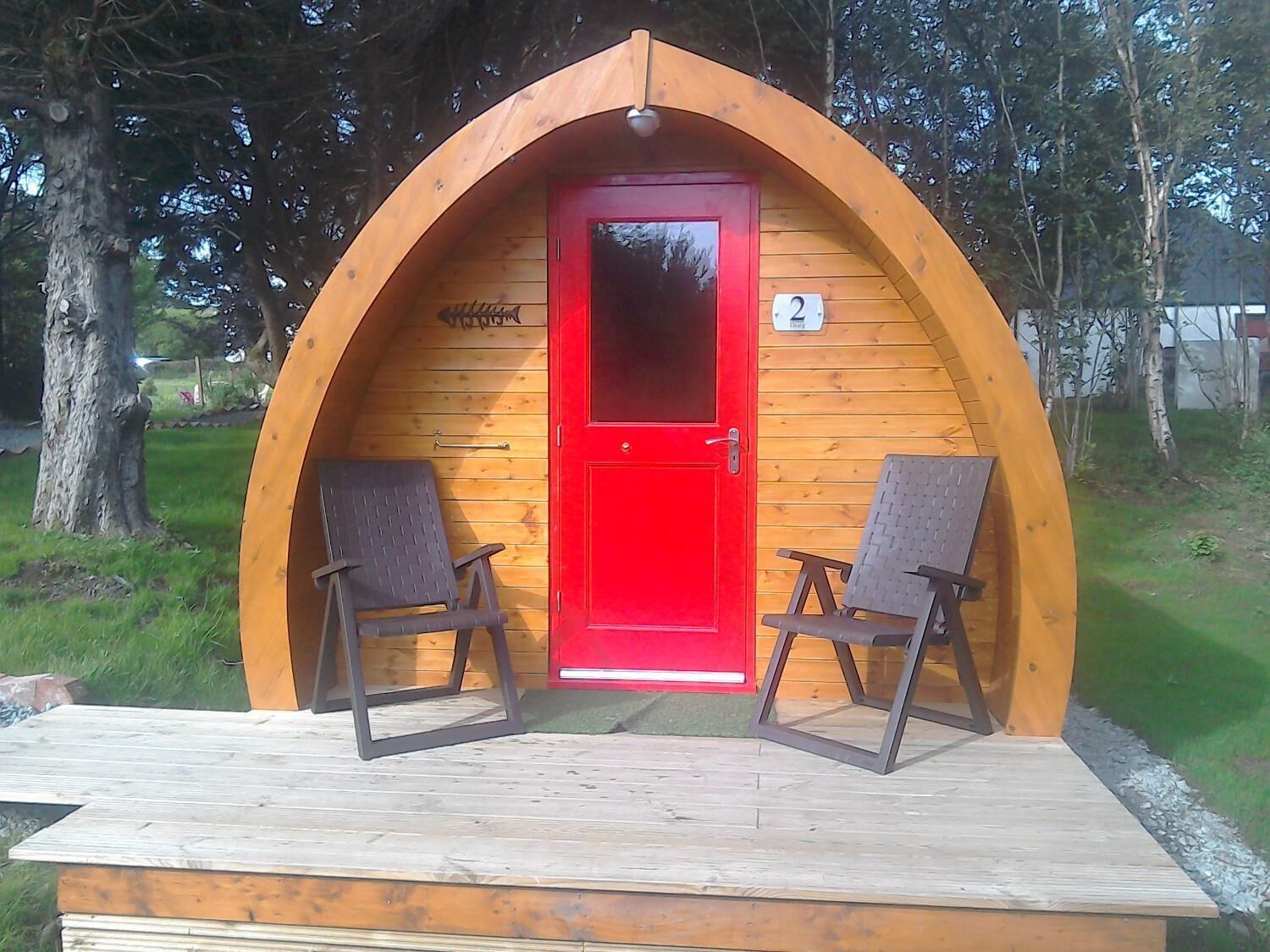 Une petite structure en bois à arc, avec une porte rouge, deux chaises et un panneau portant le chiffre « 2 ».