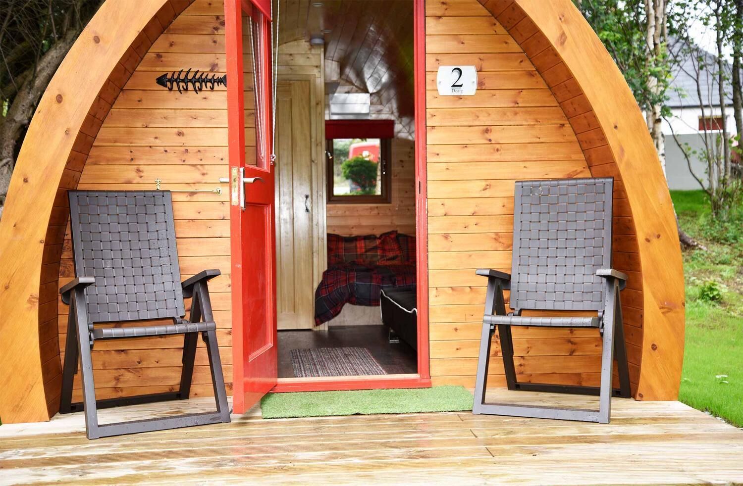 Een houten hutje met twee stoelen voor een rode deur, een '2' op de muur en een klein raam.