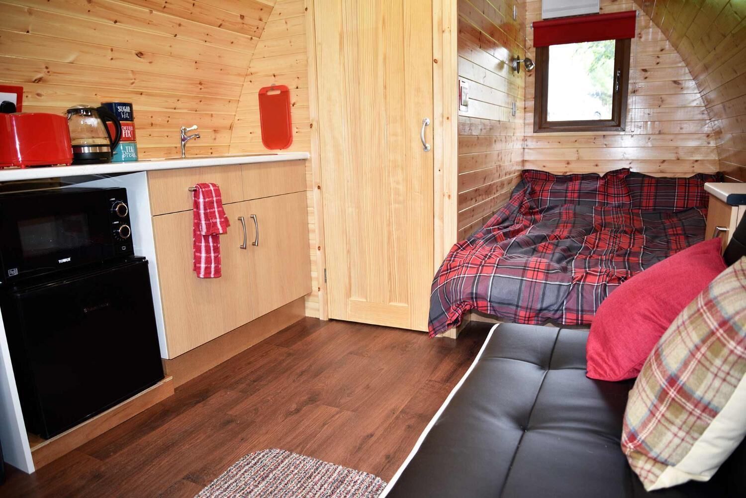 Un intérieur de chalet chaleureux comprenant un coin cuisine, un espace repas et un coin nuit avec un canapé et une fenêtre.