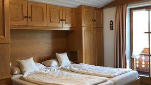 A double bed with a wooden headboard, a built-in bench at the foot of the bed, and a ceiling light fixture. - Haus am Gletscherfeld (Reit im Winkl)