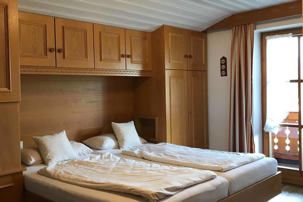 A double bed with a wooden headboard, a built-in bench at the foot of the bed, and a ceiling light fixture.