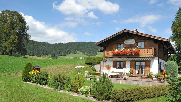 A traditional chalet with a balcony, surrounded by lush greenery and a mountainous backdrop. - Haus am Gletscherfeld (Reit im Winkl)