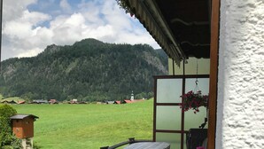 A balcony with a table and chairs, overlooking a green field and a mountain. - Haus am Gletscherfeld (Reit im Winkl)