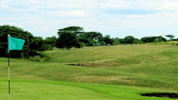 Um campo de golfe com bandeira, árvores e terreno ondulado.
