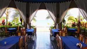 An outdoor dining area with tables and chairs, a view of the beach, and tropical plants. - Suite Rivas 126 Gran Pacifica Resort (Villa El Carmen)