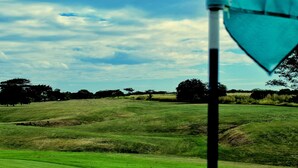 A golf course with a flagstick in the foreground, rolling green hills, and scattered trees in the background. - Suite Rivas 126 Gran Pacifica Resort (Villa El Carmen)