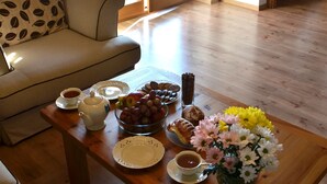 A living room with a sofa, a coffee table with breakfast items, and a view of the outside through a sliding glass door. - Apartament Gorski z Panorama Tatr (Bialy Dunajec)