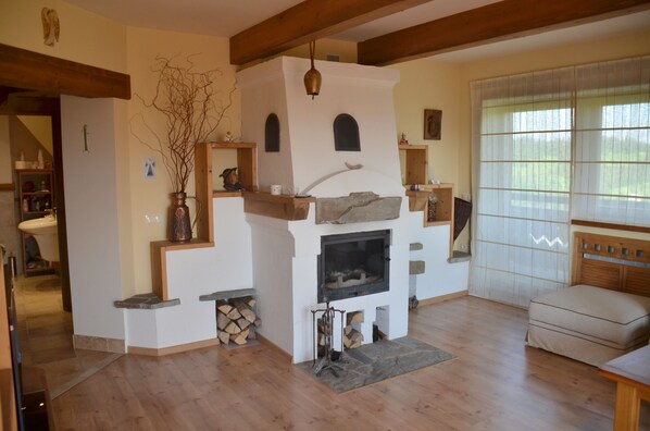 A cozy living room with a fireplace, wooden beams, and a large window.