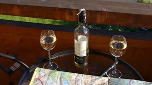 A table with a bottle of wine, two wine glasses, and a map on a balcony overlooking a house and mountains. - Apartament Gorski z Panorama Tatr (Bialy Dunajec)