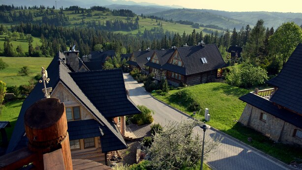 A row of traditional wooden houses with sloped roofs, surrounded by lush green fields and mountains in the background. - Apartament Gorski z Panorama Tatr (Bialy Dunajec)