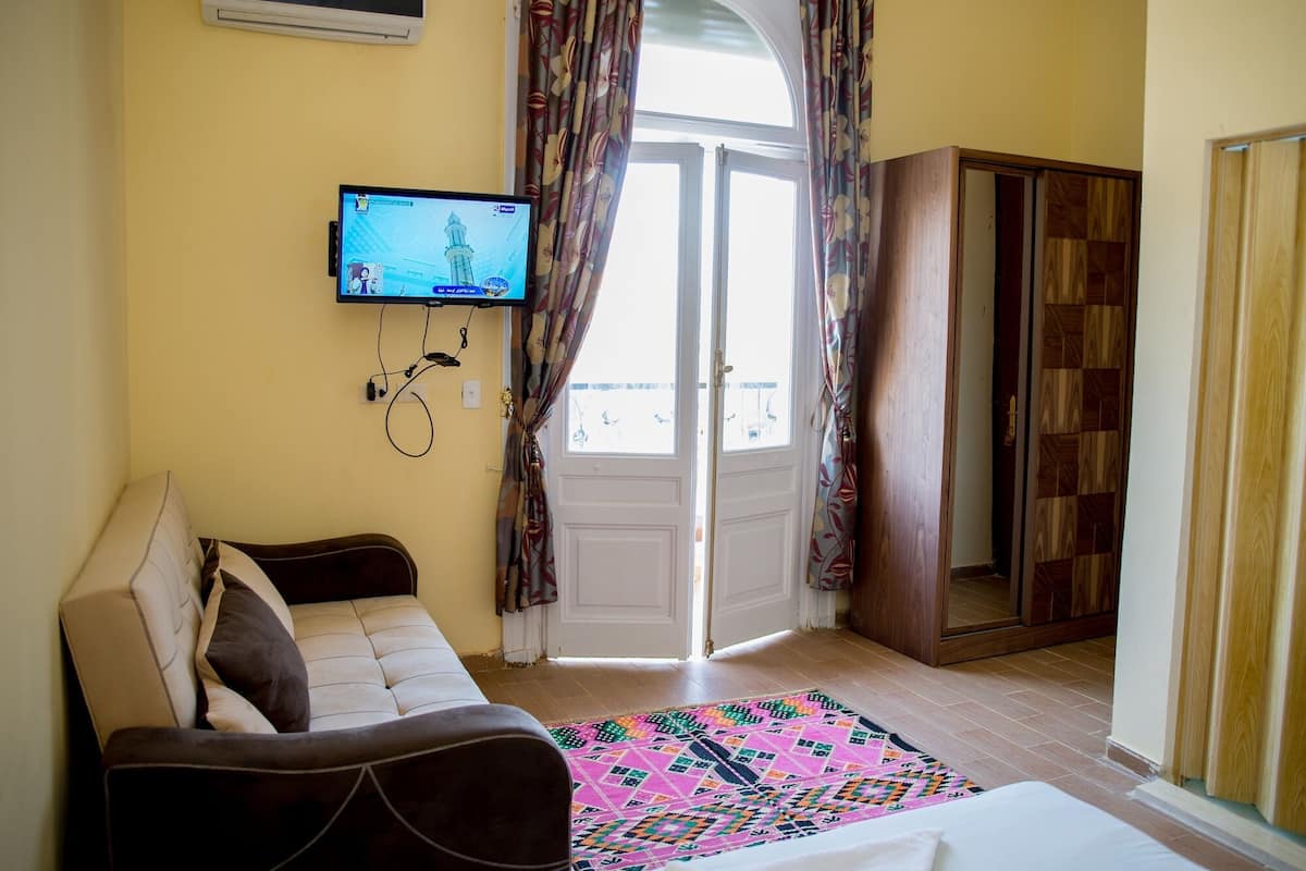 Ein Zimmer mit einer Couch, einem an der Wand befestigten Fernseher, einem gemusterten Teppich und einem Holzschrank.