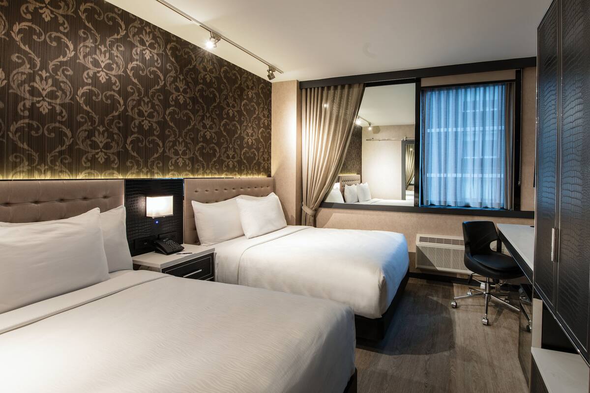 Camera d'albergo con due letti, una scrivania, una sedia, un'ampia finestra con tende e una parete decorata.