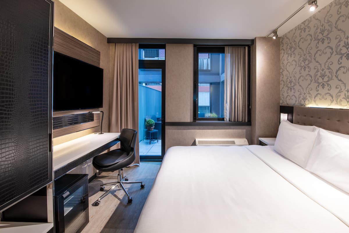 Camera d'albergo con un letto grande, una scrivania con una sedia, una TV a schermo piatto e una finestra con tende.