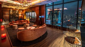 A modern lounge with a curved sofa, round tables, and a city view. - Aliz Hotel Times Square (New York)