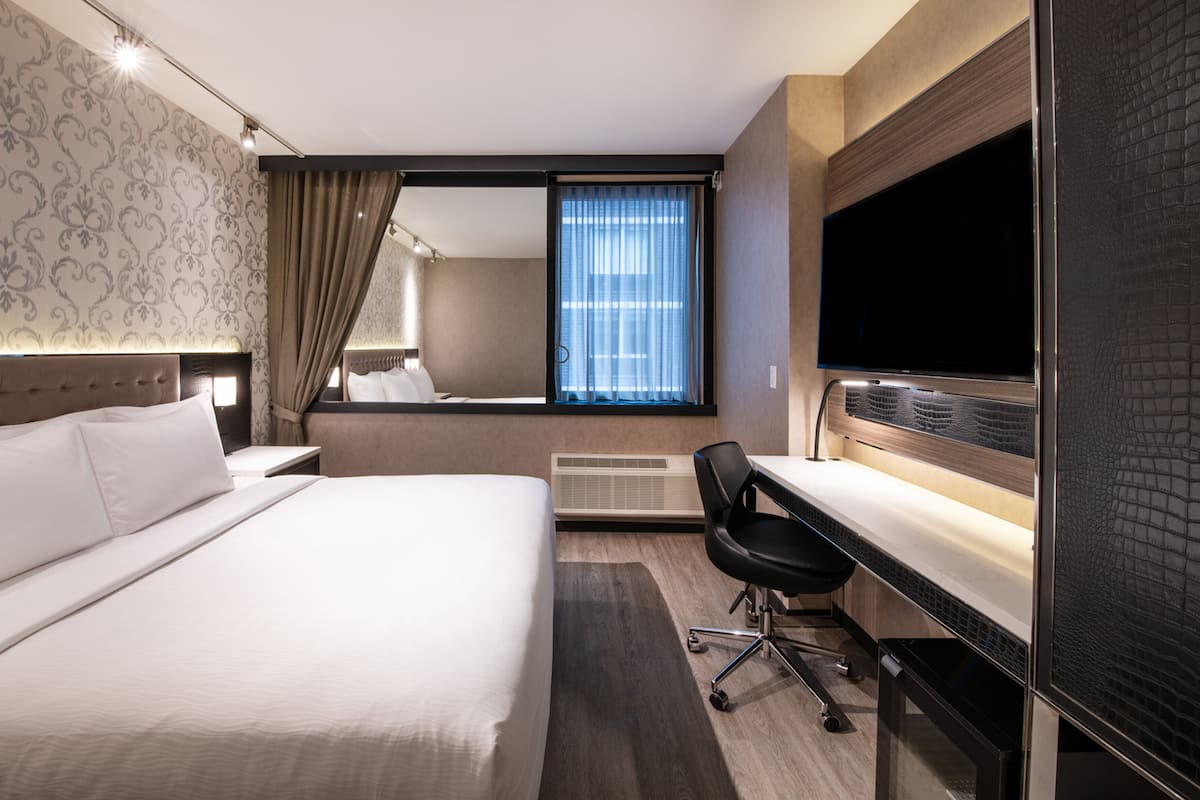 Una camera d'albergo con un letto grande, una scrivania con una sedia, una televisione a schermo piatto e una finestra con tende.