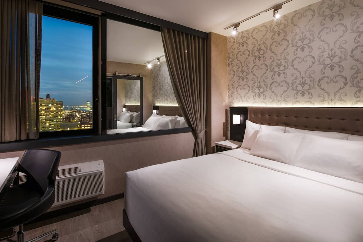 Camera d'albergo con un letto grande, una scrivania, una sedia, uno specchio e vista sulla città.