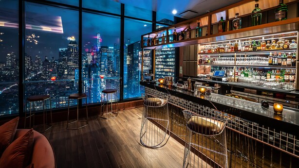 A bar with a city view, wooden floors, and metal bar stools. - Aliz Hotel Times Square (New York)