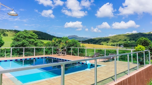 Una piscina con cubierta de madera y barandilla de metal, rodeada de exuberante vegetación y colinas al fondo.