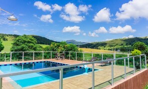 A swimming pool with a wooden deck and metal railing, surrounded by lush greenery and hills in the background. - Alecrim do Campo - Casa para 12 pessoas com 3 quartos (Guape)