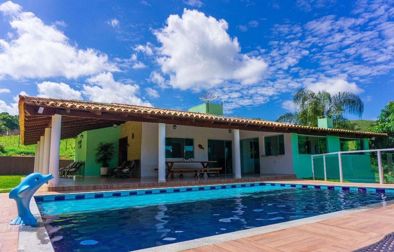A swimming pool with a covered patio area, a green building with large windows, and a clear blue sky.