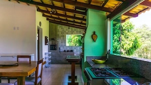 Una cocina con estufa a gas, mesa de comedor de madera, sillas y una ventana con vistas al verdor.