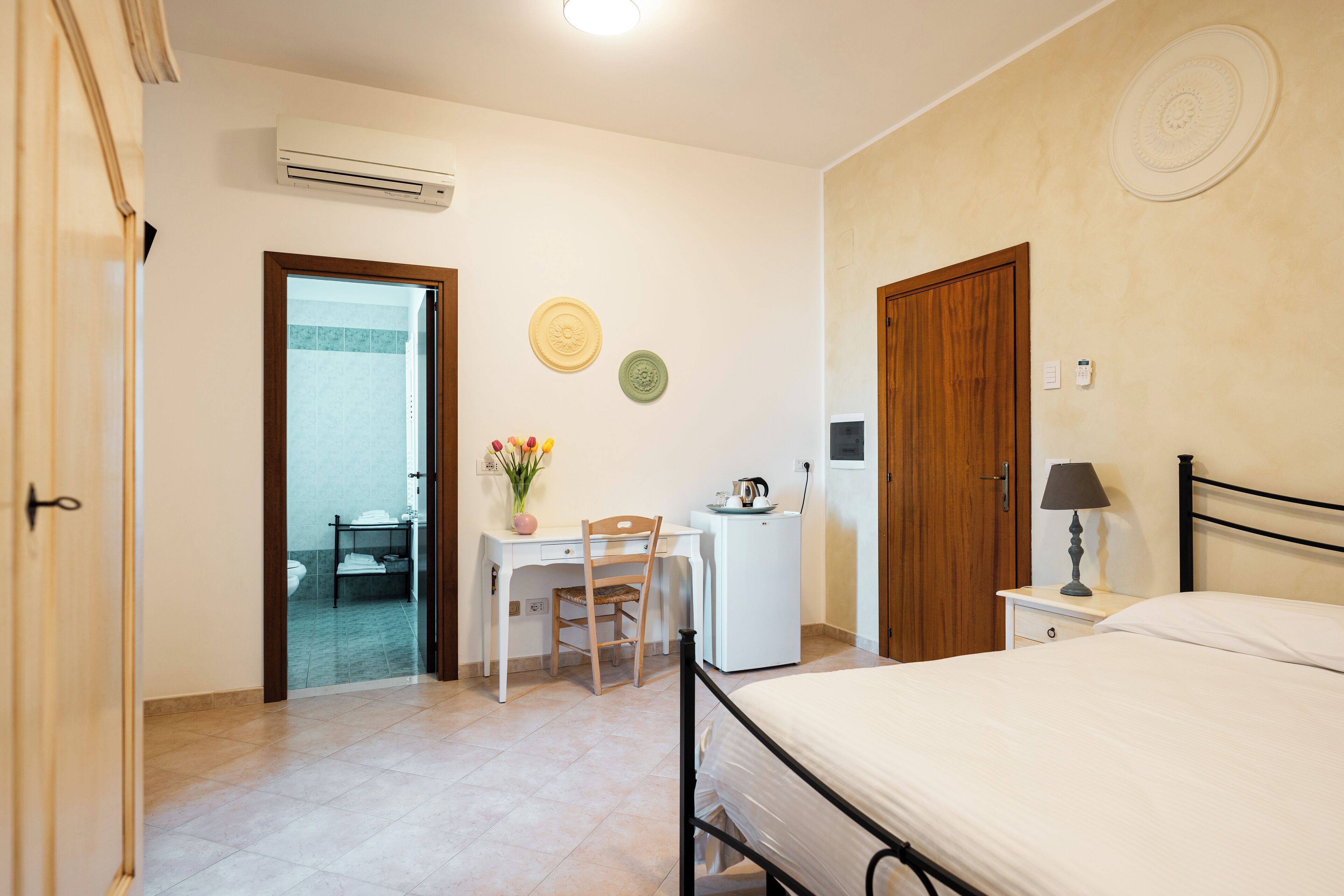 Un dormitorio con cama, escritorio con silla, refrigerador pequeño y aire acondicionado instalado en la pared.