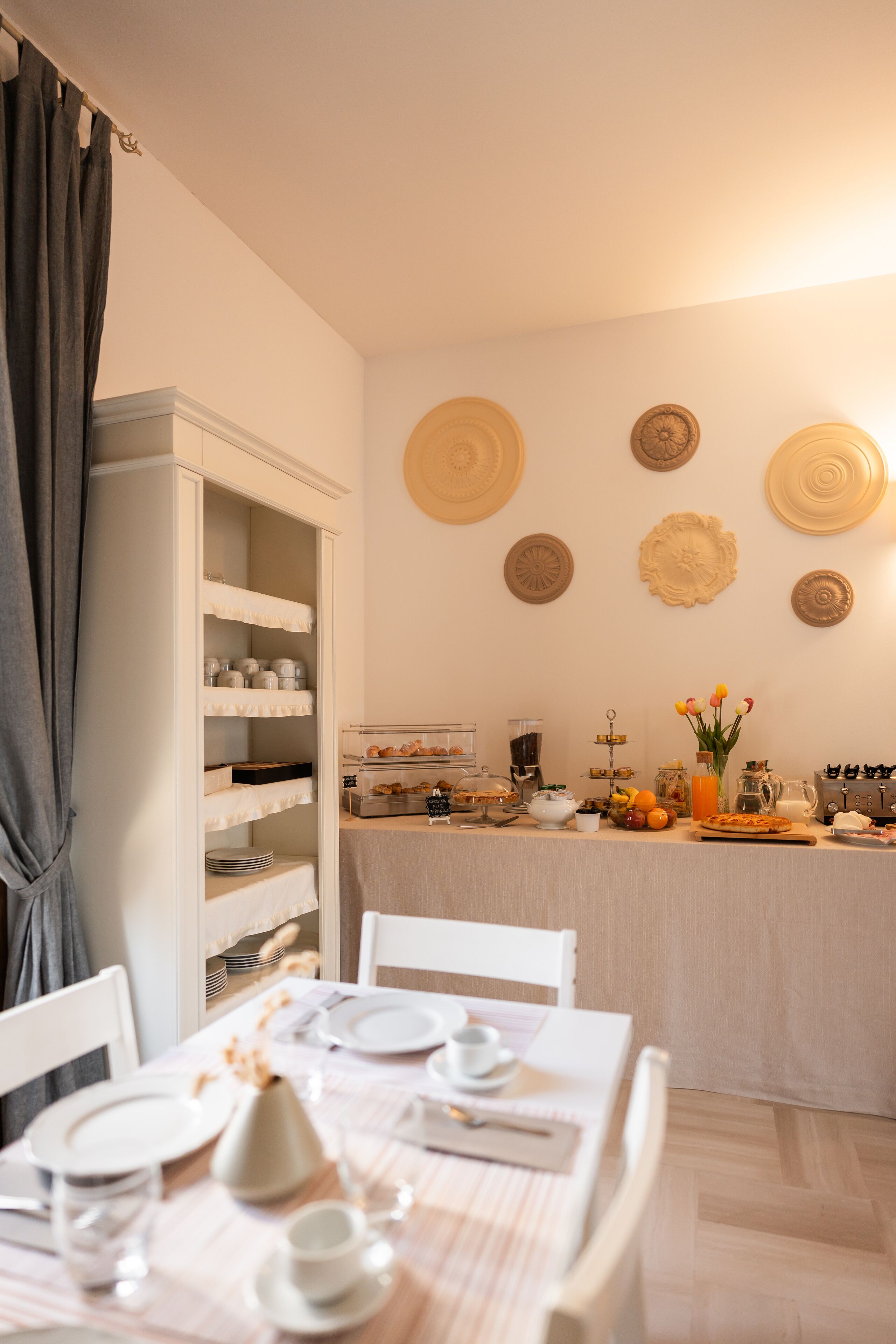 A dining area with a table set for four, a buffet counter with various food items, and a white cabinet with shelves.