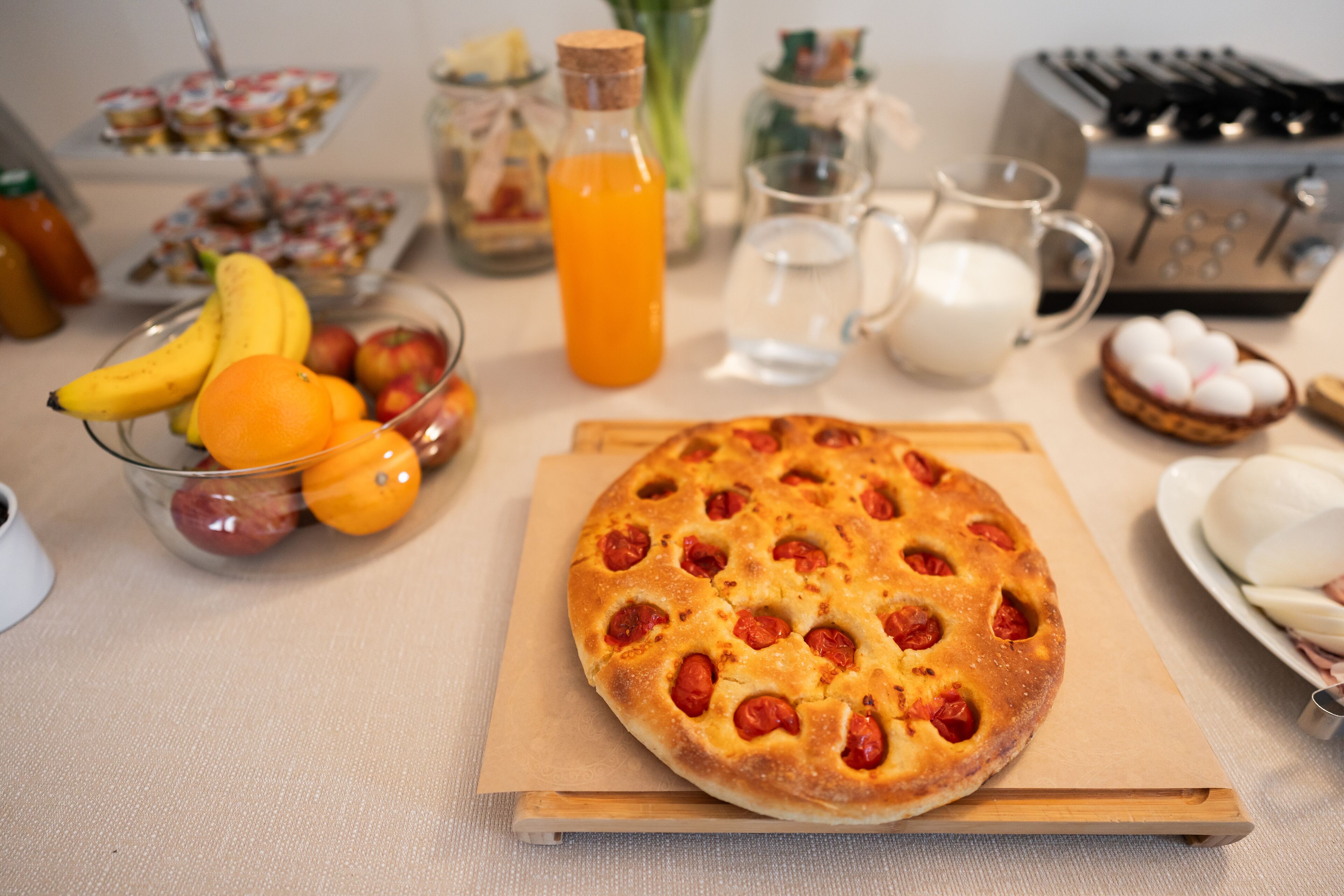 Ein Frühstückstisch mit Pizza, Obstschale, Saft, Milch und einem Toaster.