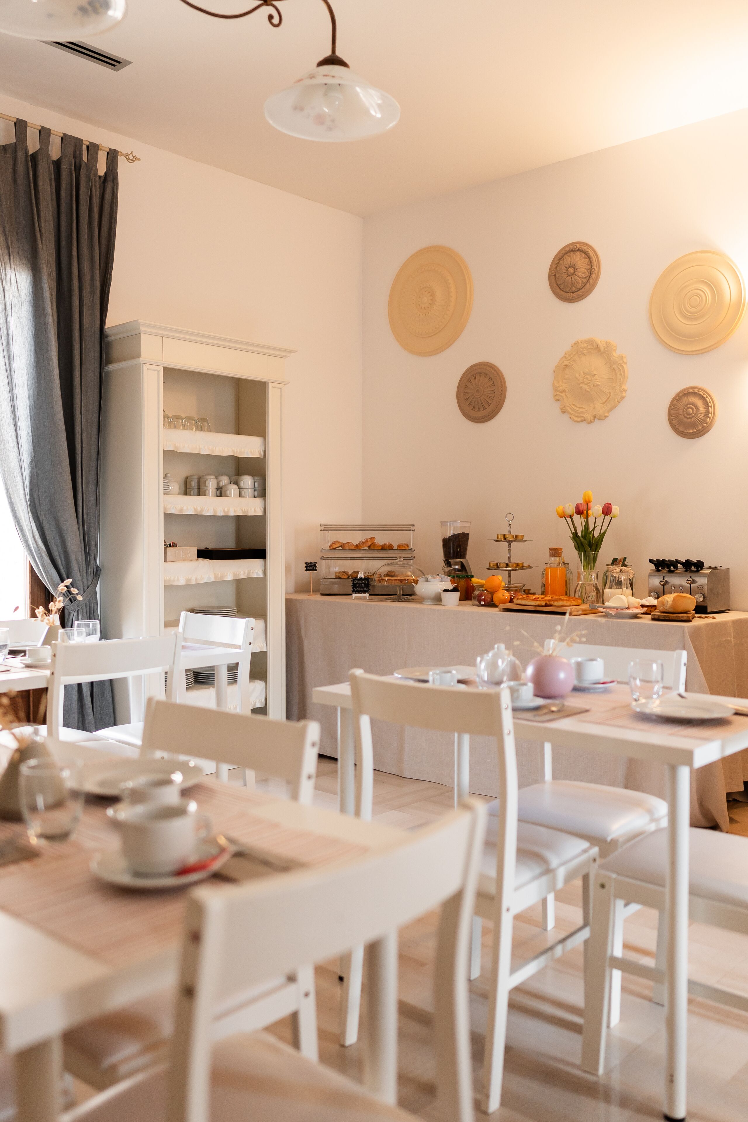 Un espace repas avec des meubles blancs, un buffet proposant divers plats et des assiettes décoratives accrochées au mur.