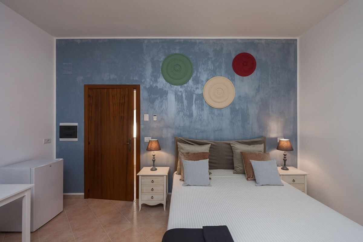 A bedroom with a bed, bedside tables, a dresser, a door, and wall decorations.