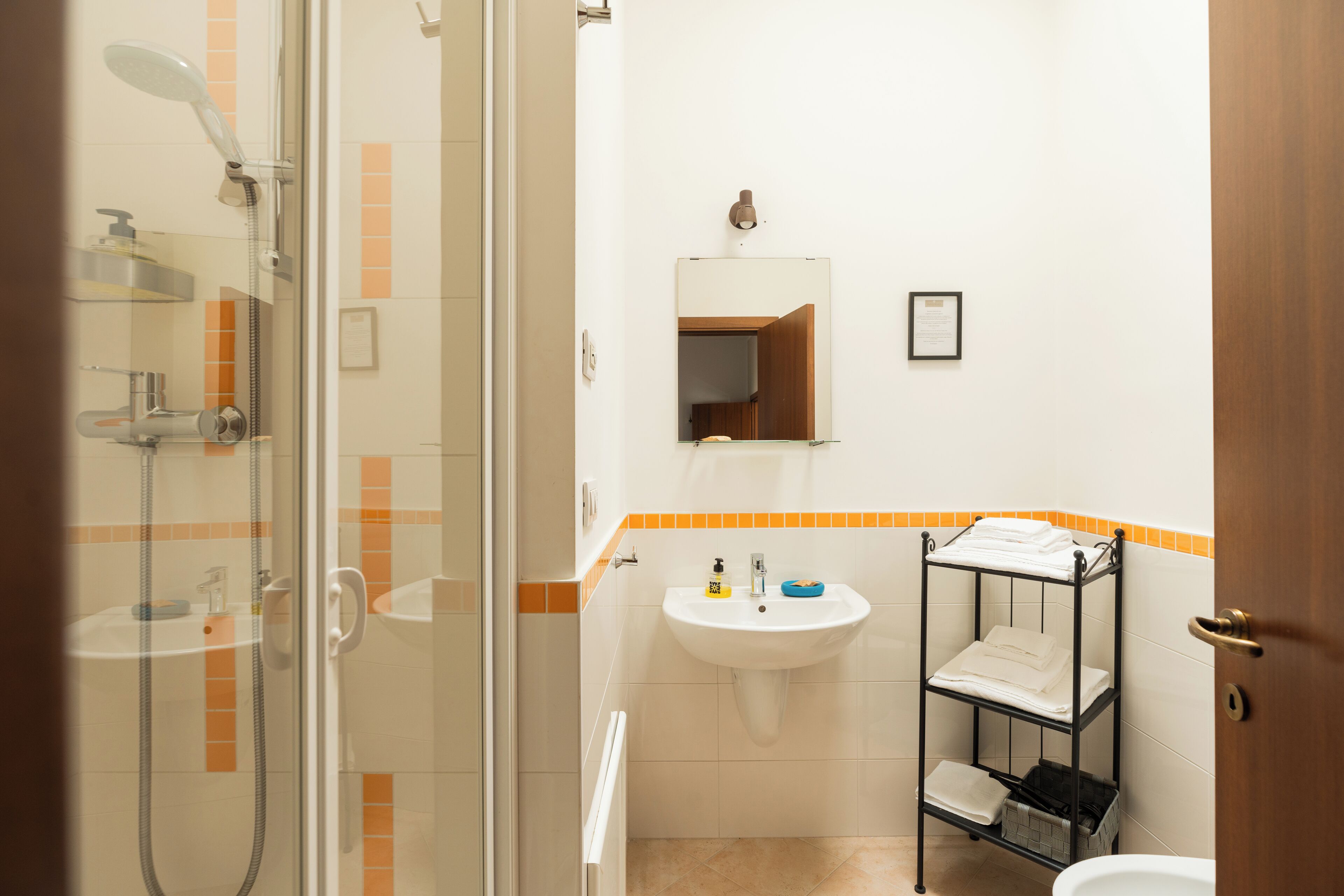 Un baño con ducha de vidrio, un lavamanos con espejo y un perchero con toallas dobladas.