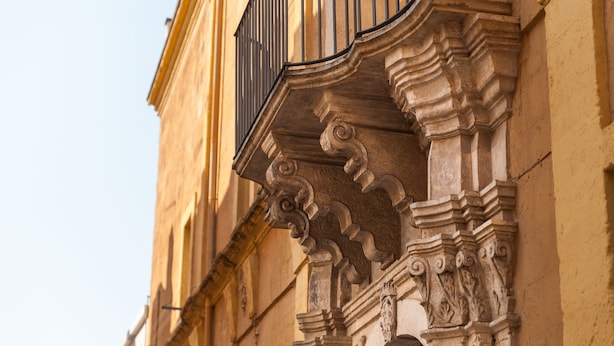 A close-up of ornate architectural details including carved stonework and a metal balcony railing. - Palazzo de Luca (Fasano)